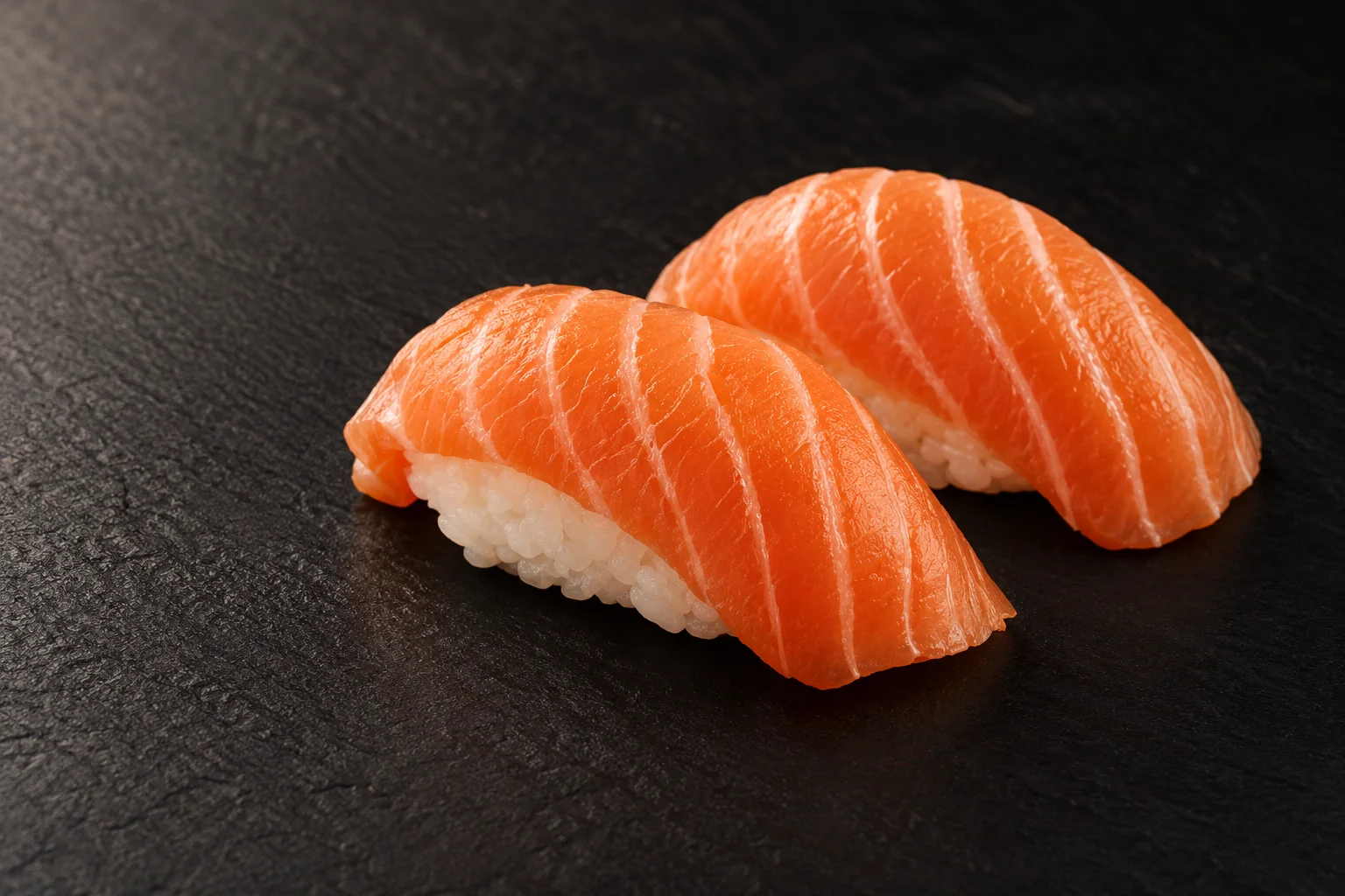 Deux sushis au saumon sur une ardoise noire.
