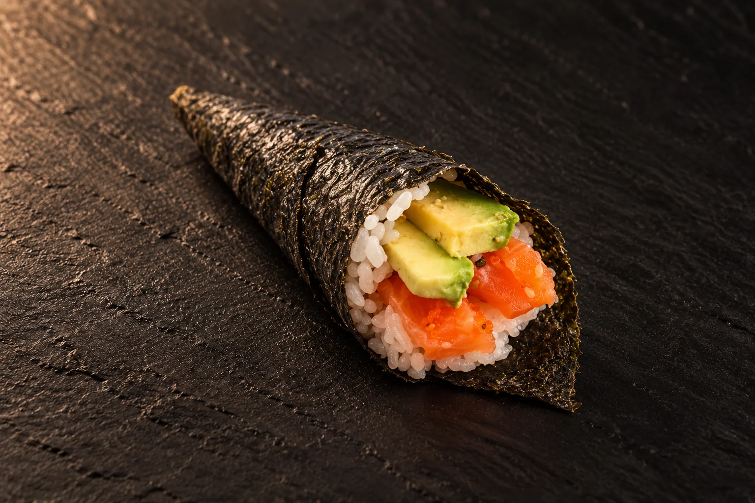Un cornet de temaki garni de saumon, d'avocat et de riz, sur une ardoise noire.